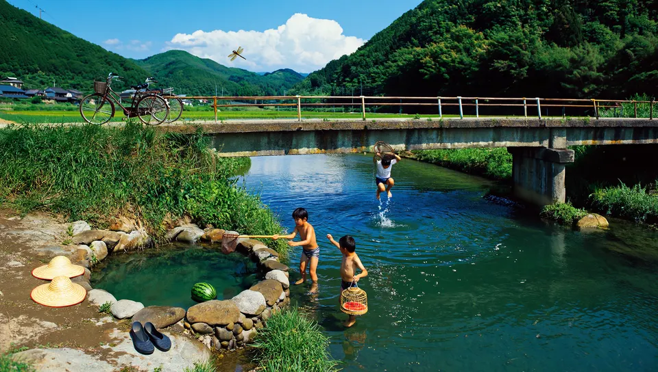 夏の昼、古いコンクリートの橋の下の澄んだ川の淵で遊ぶ子どもたち